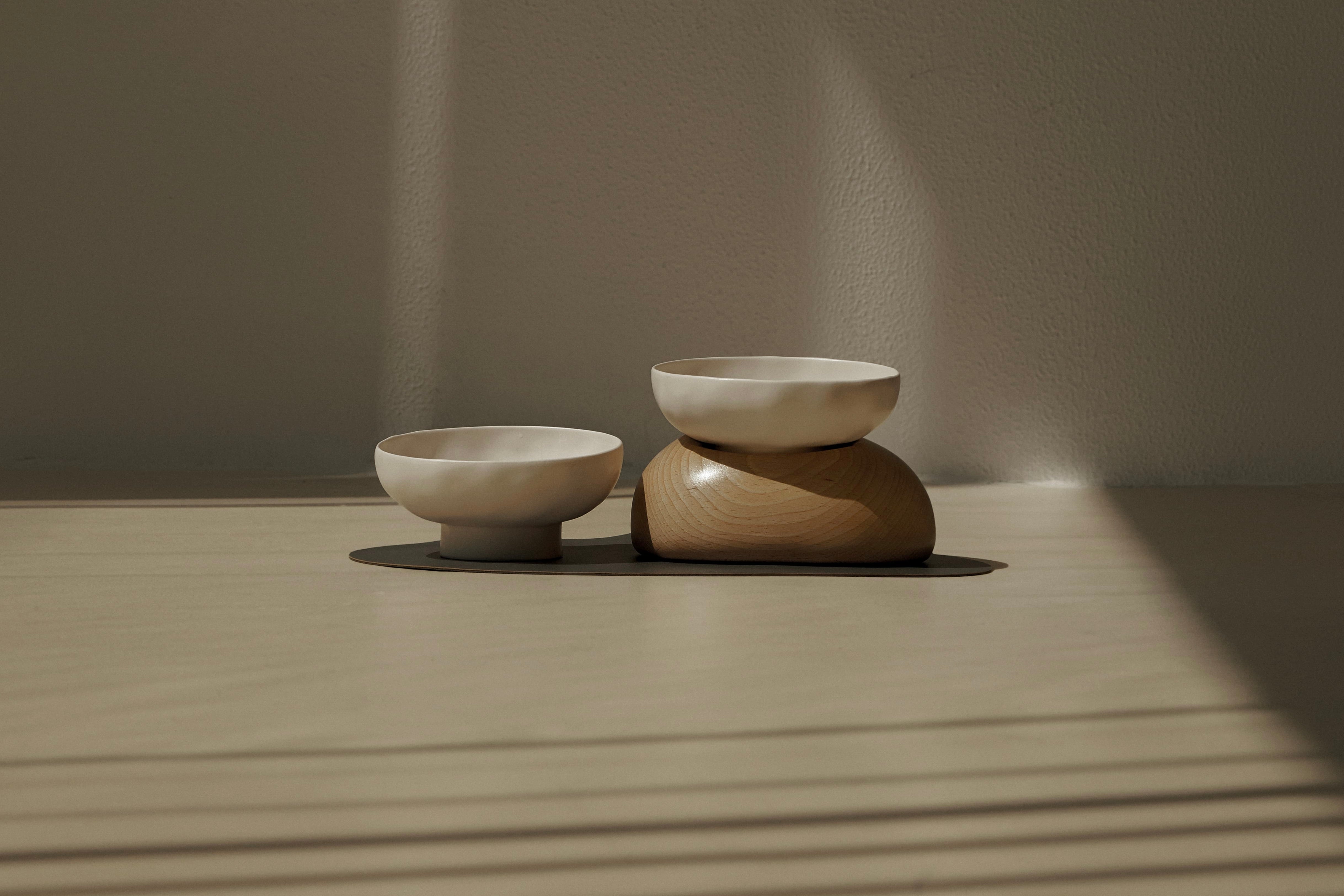 Two pebble bowls, one with a base, placed on a black mat