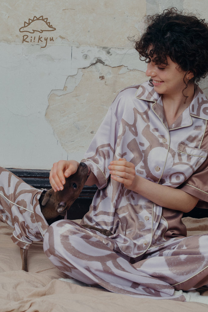 A female model pets a dog's head, both of them wear short sleeve pajama sets.