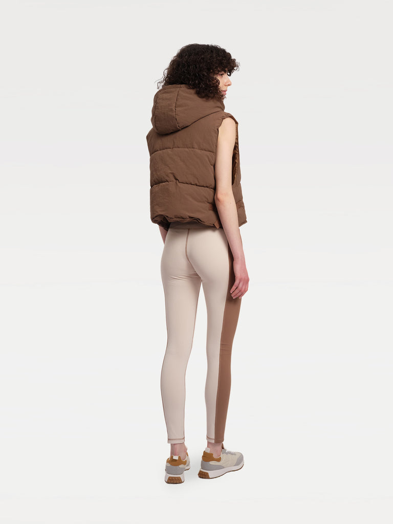 a female model wearing a brown vest and patchwork leggings, as seen from the back.