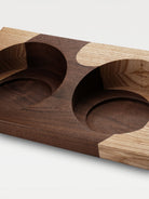 A two-tone wooden trapezoidal base with two grooves for holding bowls