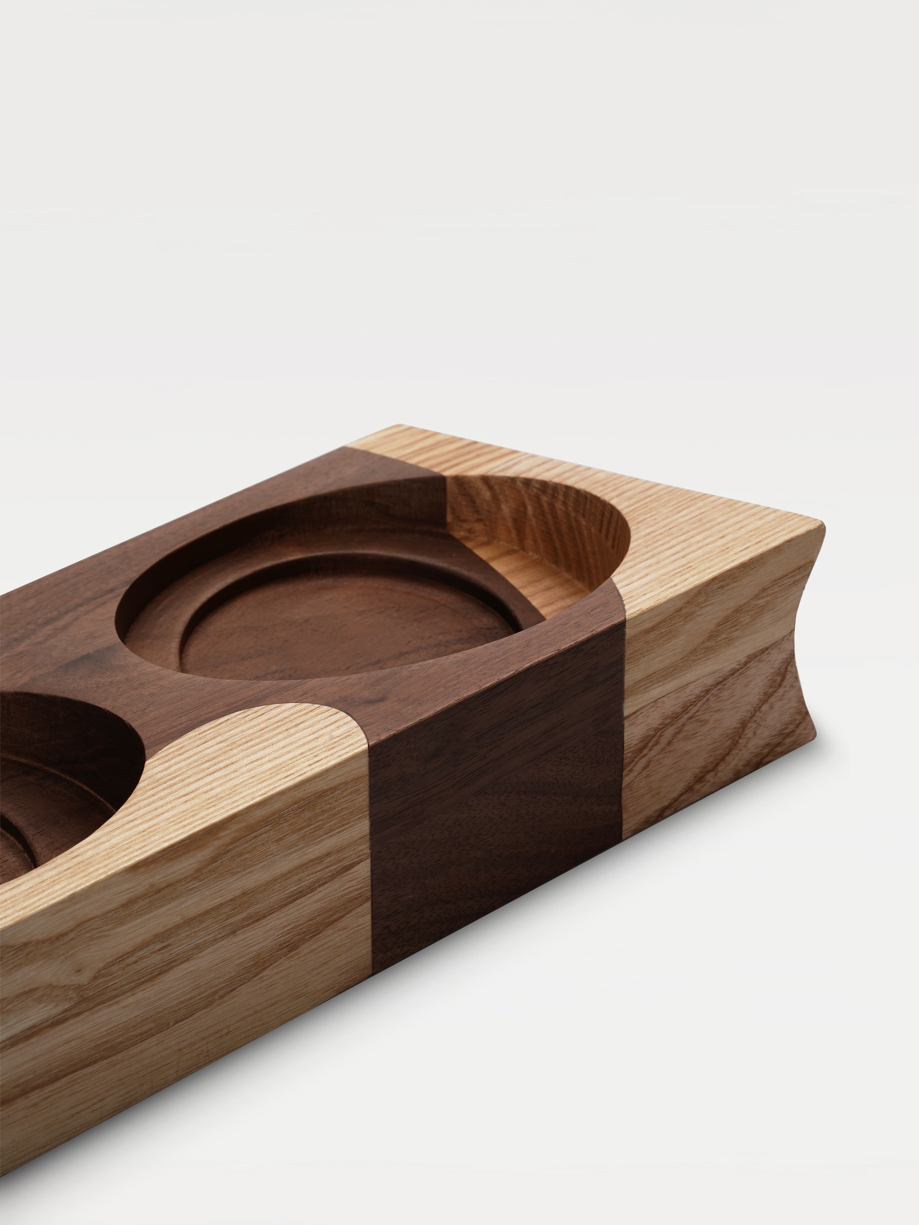 A two-tone wooden trapezoidal base with two grooves for holding bowls