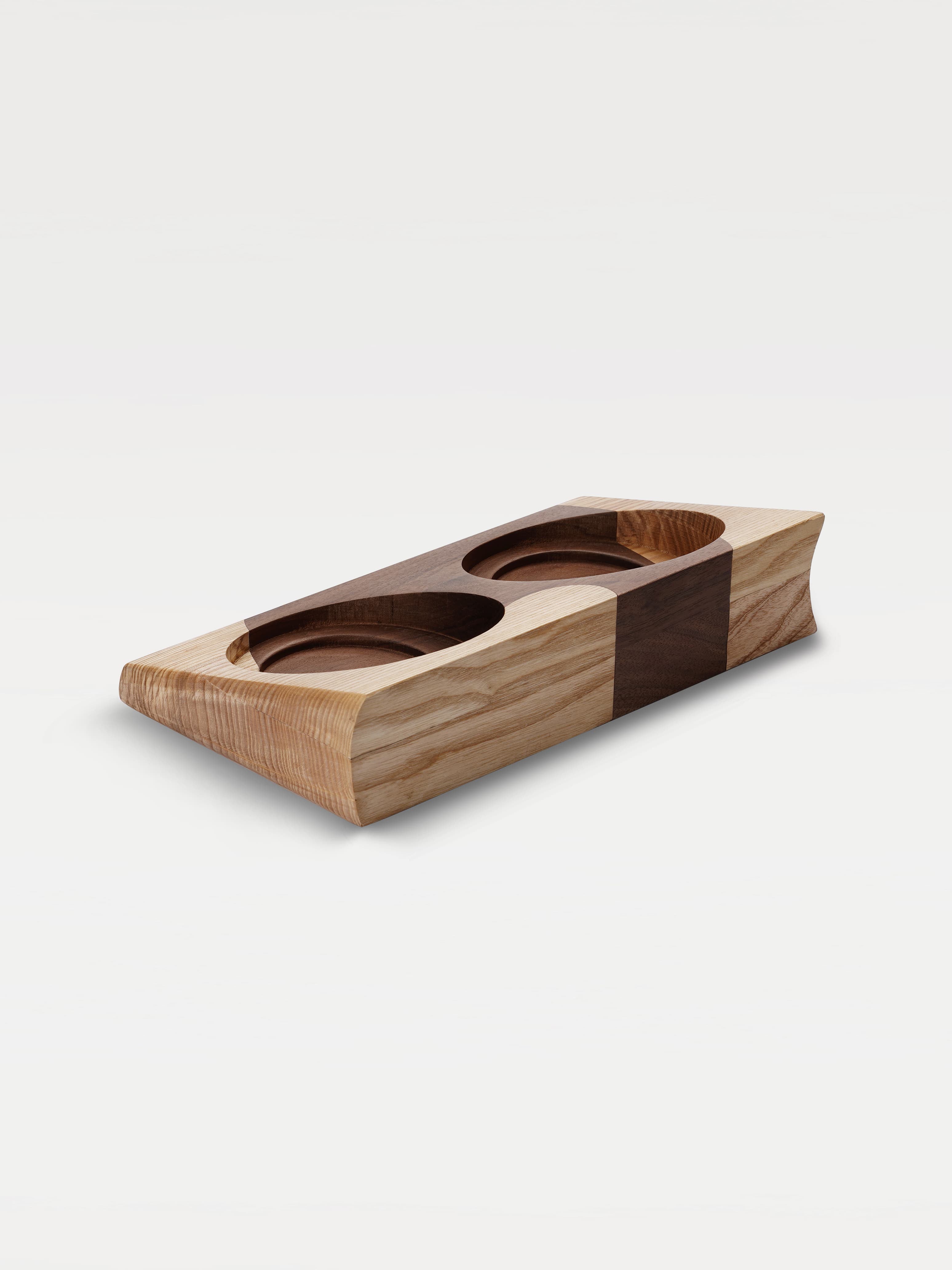 A two-tone wooden trapezoidal base with two grooves for holding bowls